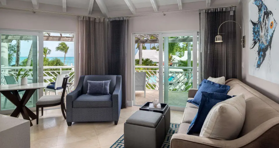Villa living area with sofa, armchair, balcony, and ocean glimpse at Beaches Turks & Caicos.
