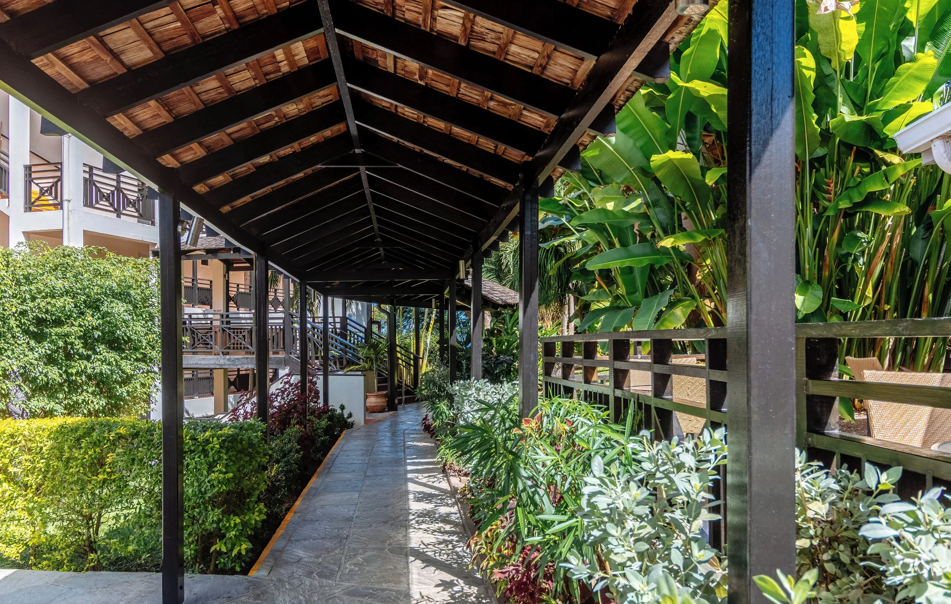 Covered garden walkway beside tropical plants and guest balconies at Bel Jou Hotel.