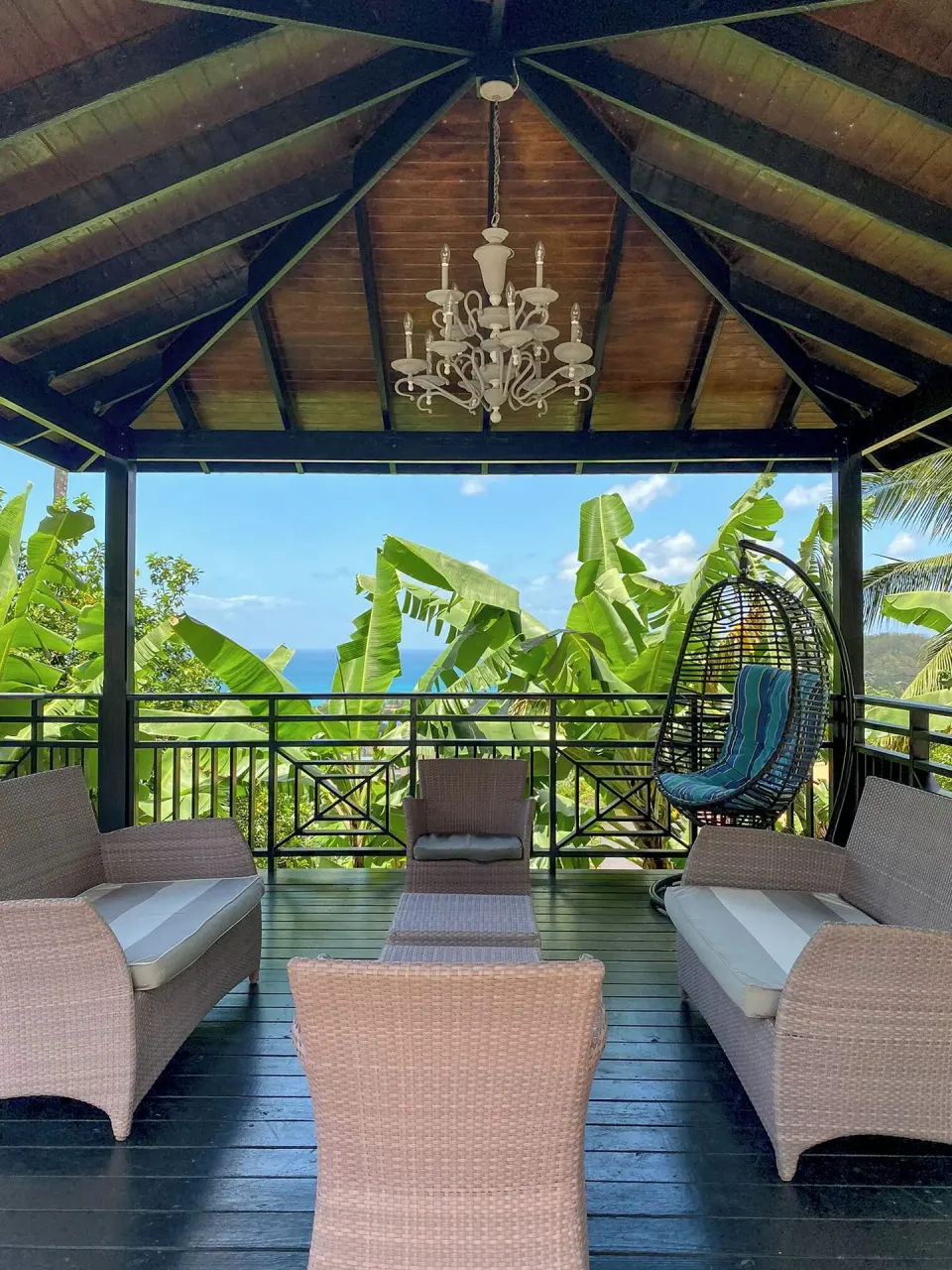 Gazebo lounge with wicker chairs, hanging seat, chandelier, and sea view at Bel Jou Hotel.