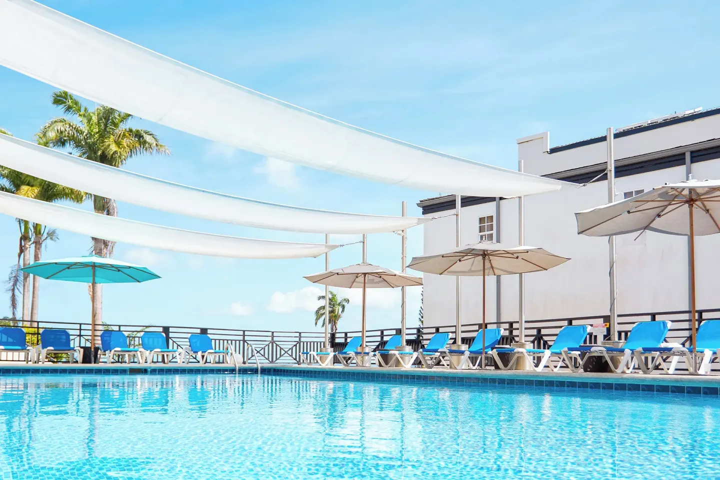 Swimming pool with blue loungers and shade sails at Bel Jou Hotel.