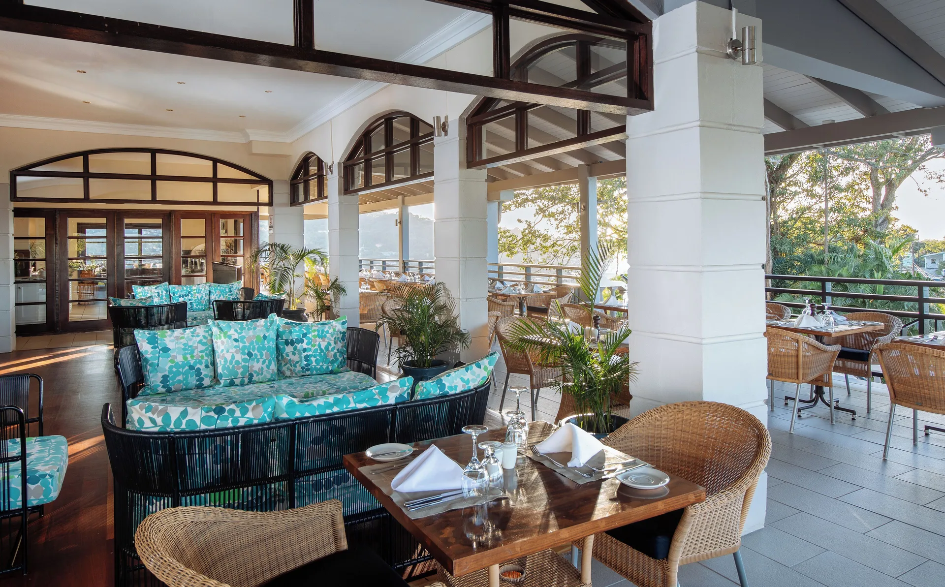 Covered restaurant terrace with wicker seating and set tables at Bel Jou Hotel.