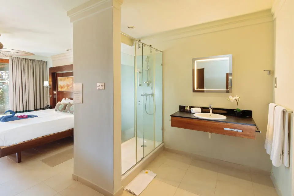Garden View room bathroom with glass shower and bed beyond at Bel Jou Hotel.