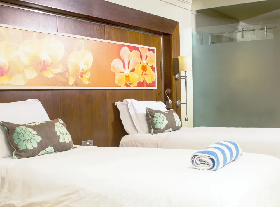 Garden View room with two beds, floral headboard art and glass shower at Bel Jou Hotel.