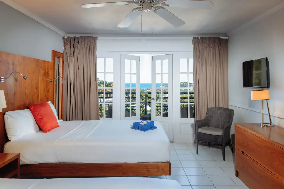 Ocean View room bed beside French doors with a visible sea view at Bel Jou Hotel.