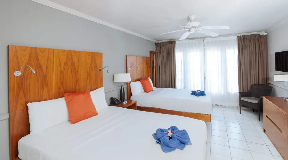 Ocean View room with two beds, dresser, armchair, and curtained doors at Bel Jou Hotel.