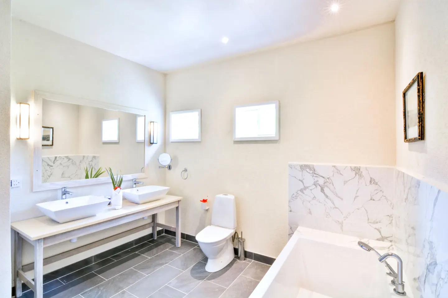 Bathroom with twin sinks, bathtub, and marble-style tile at Bequia Beach Hotel.