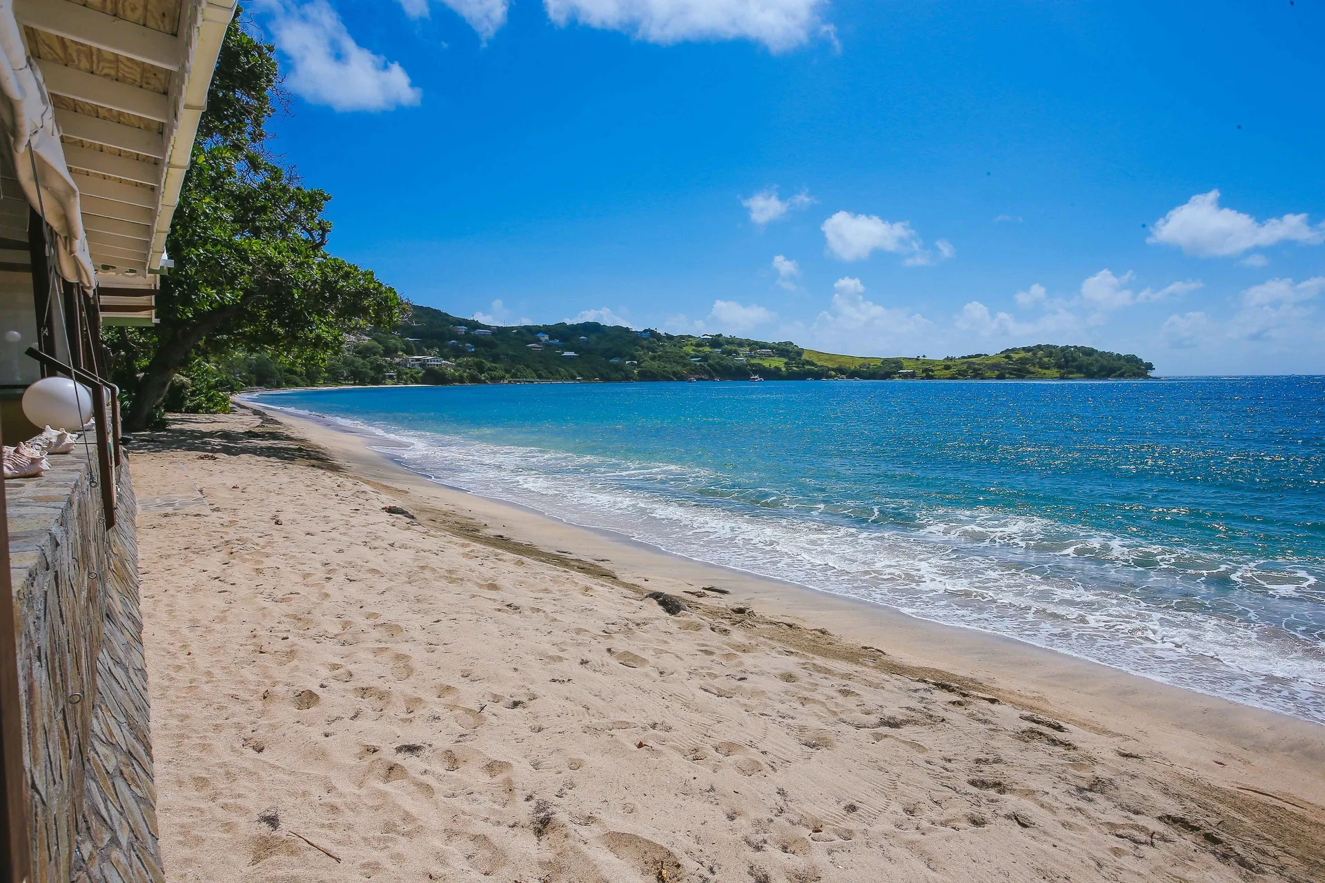 Sandy beach and blue bay beside a stone building at Bequia Beach Hotel.