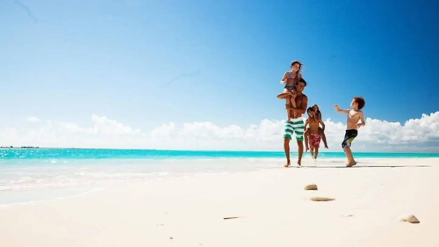Family walking on a bright sandy beach by turquoise water at Bequia Beach Hotel.