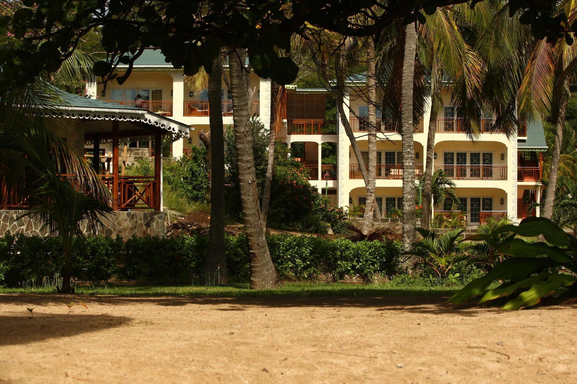 Garden buildings and balconies are seen through palm trees at Bequia Beach Hotel.