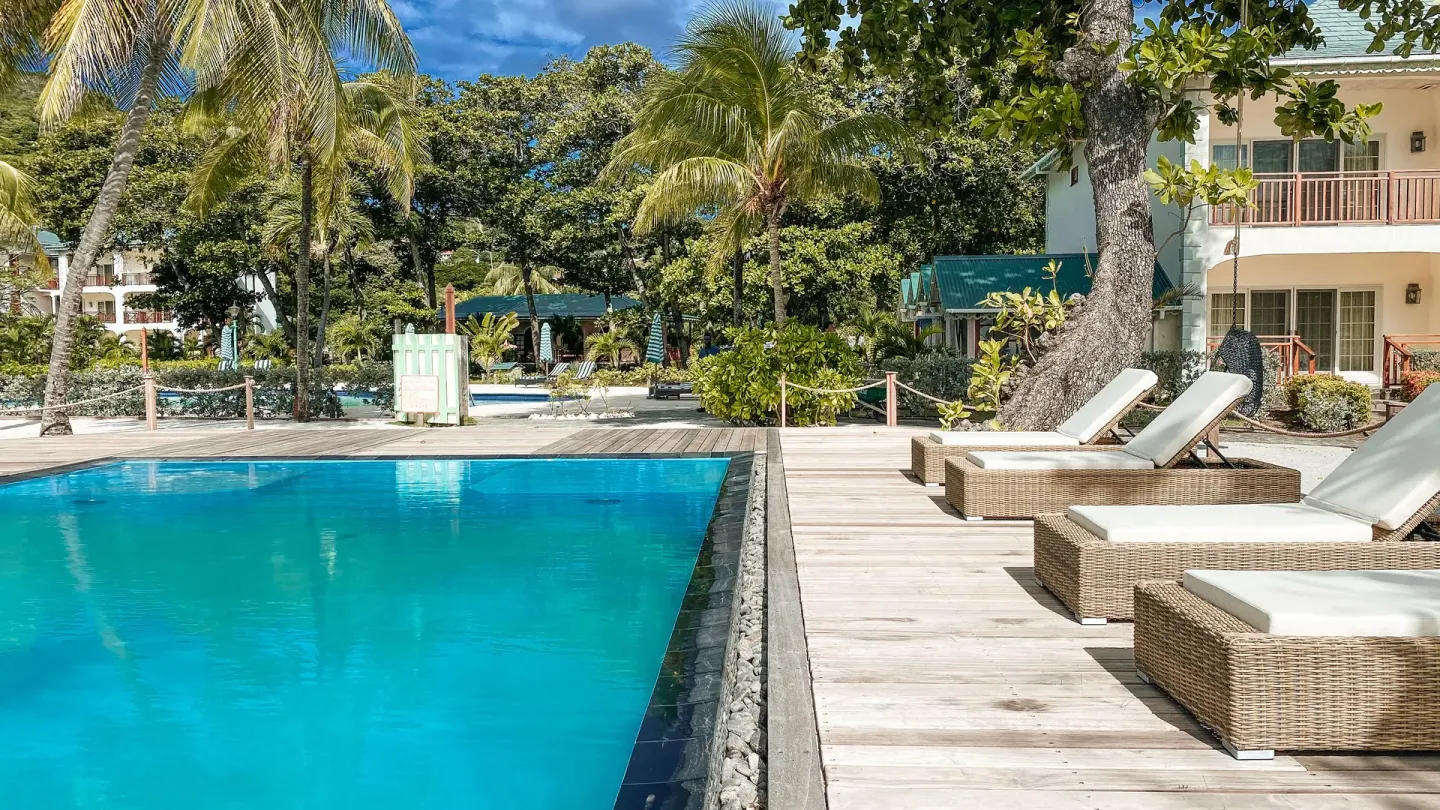 Quiet pool deck with wicker loungers, palms and guest buildings at Bequia Beach Hotel.