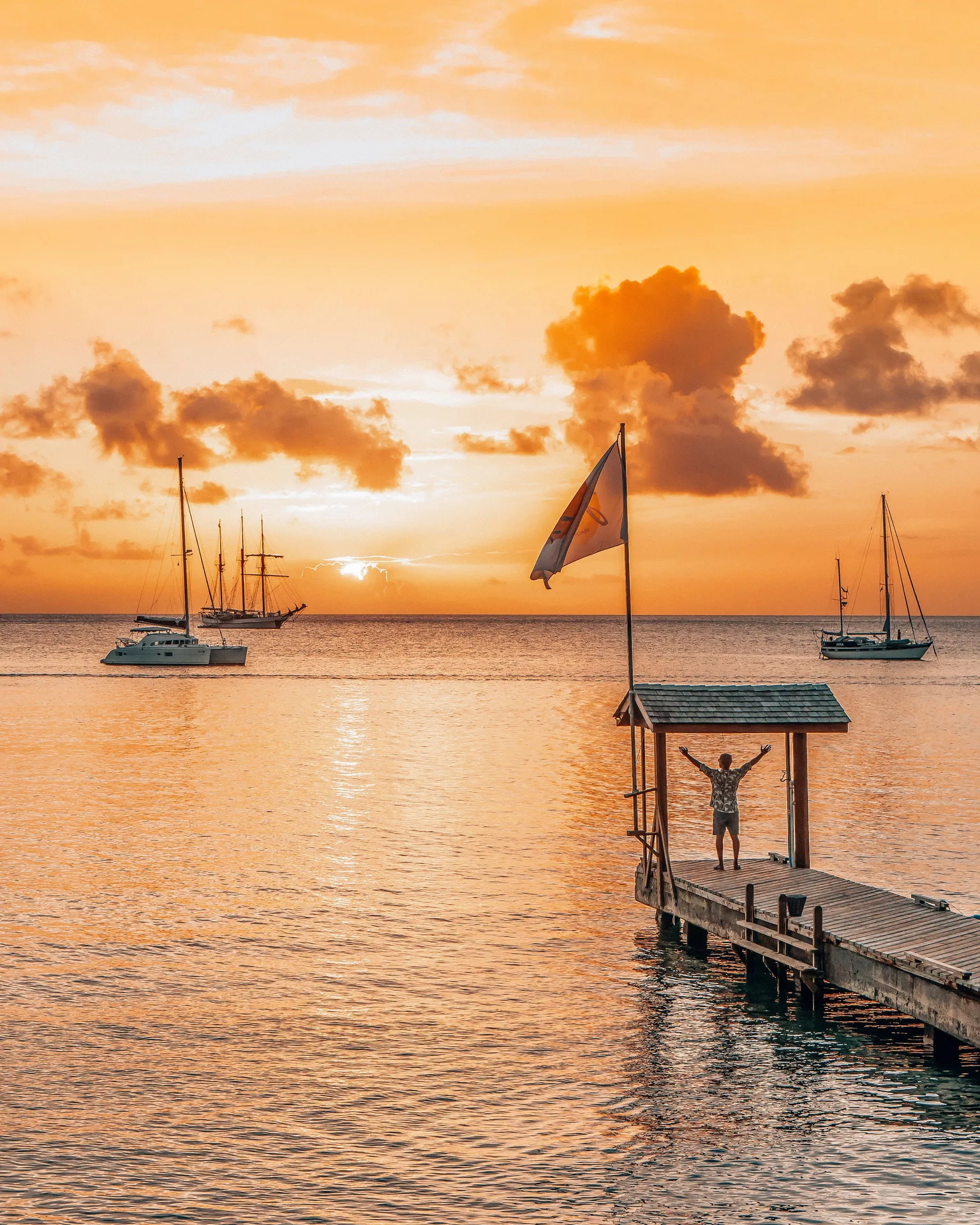 A wooden jetty, sailboats and orange sunset over the water at Bequia Beach Hotel.