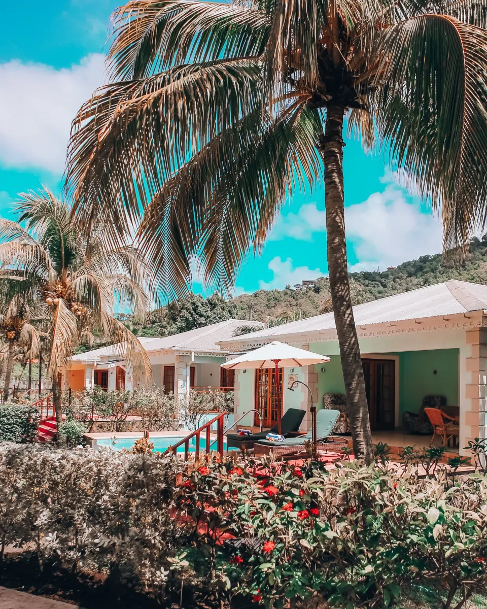 Palm-shaded cottages with private pools at Bequia Beach Hotel viewed across tropical gardens.