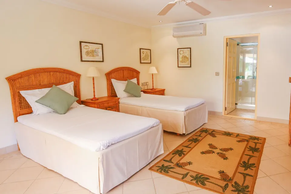 Twin-bed bedroom in a two-bedroom cottage at Bequia Beach Hotel with an open bathroom doorway.