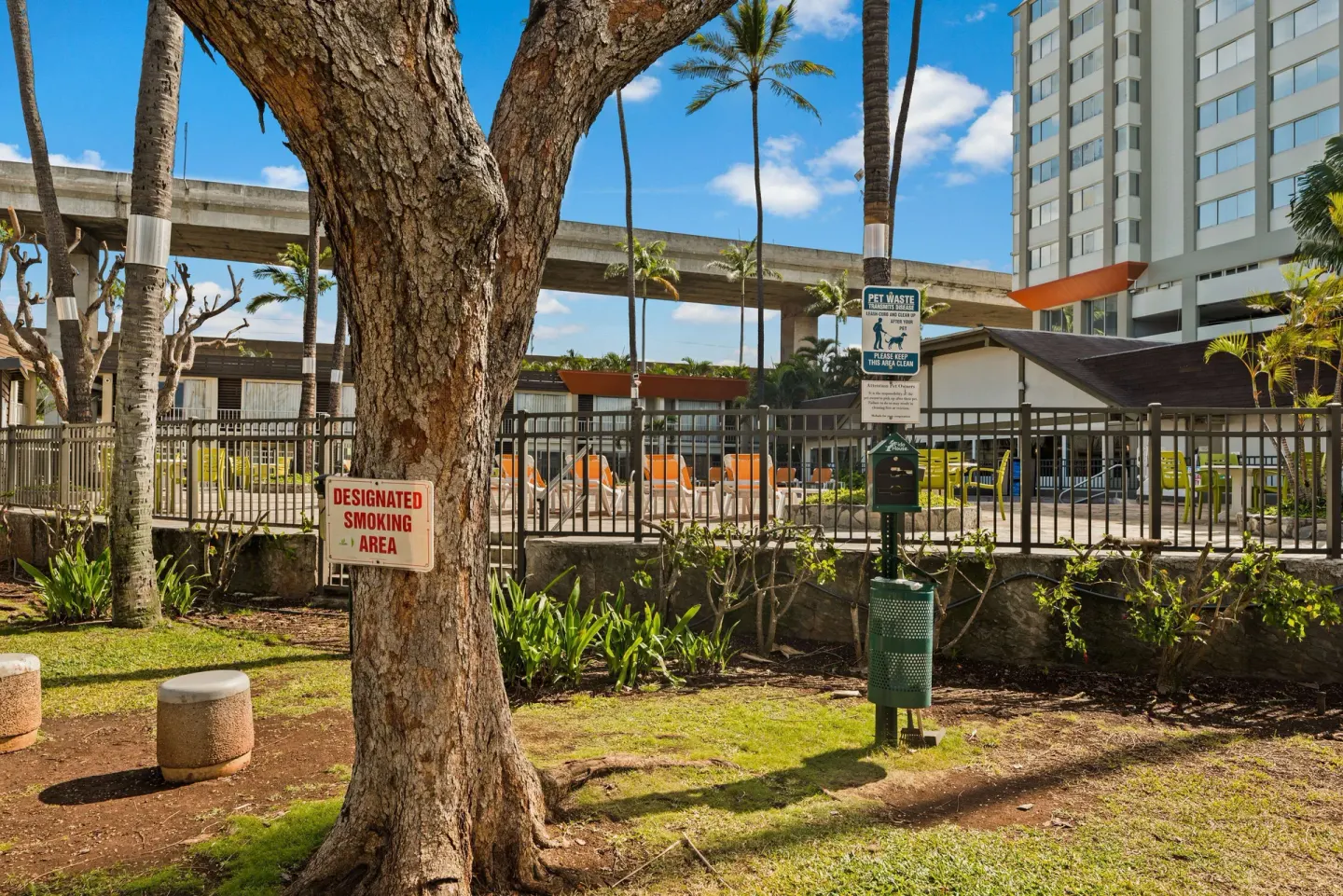 Tree-shaded outdoor area with smoking and pet waste signs at Best Western The Plaza Hotel Honolulu Airport.