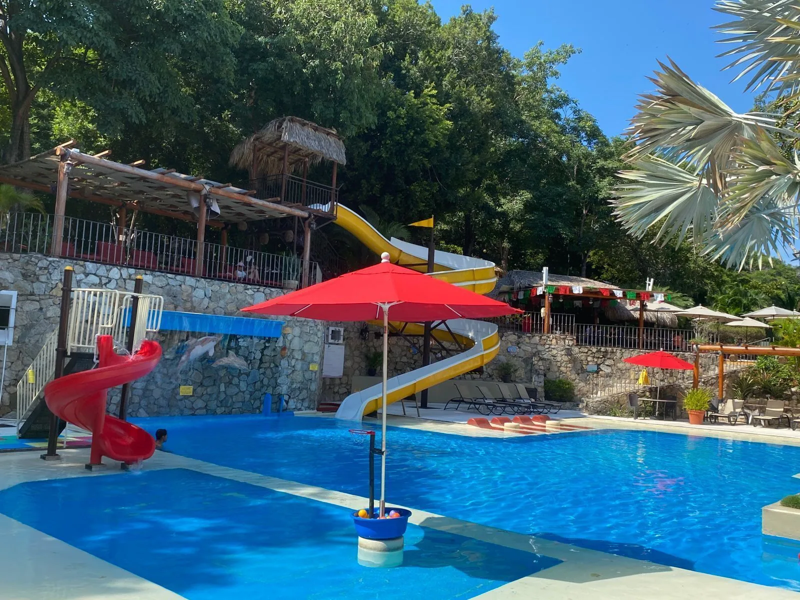Family pool with slides and red umbrella at Binniguenda Huatulco & Beach Club.
