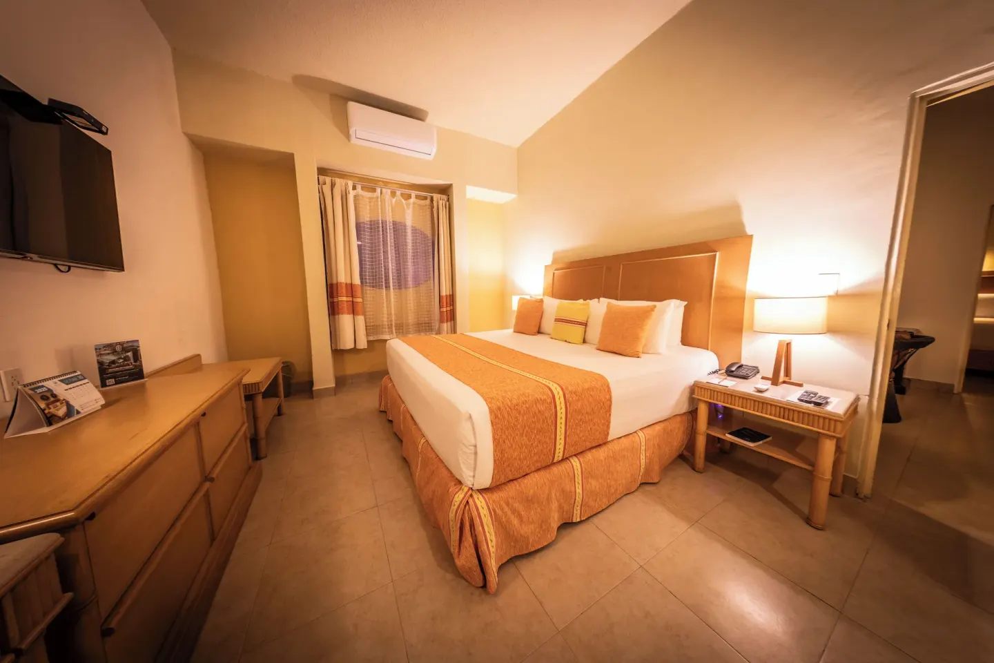 King bed guest room at Binniguenda Huatulco & Beach Club with dresser, TV, mirror, and bedside lamp.