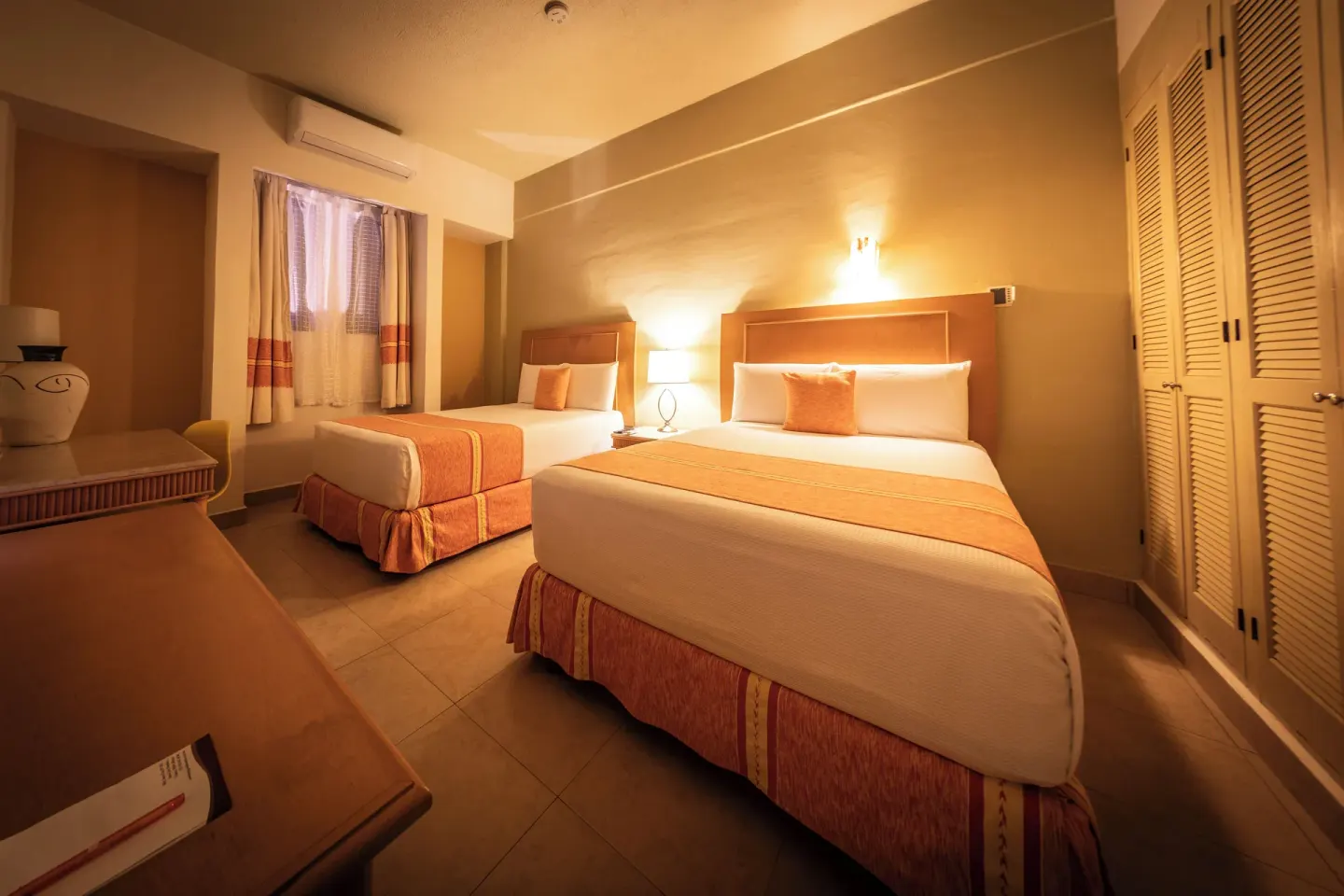 Guest room with two beds at Binniguenda Huatulco & Beach Club, showing closets, dresser, and warm lamps.