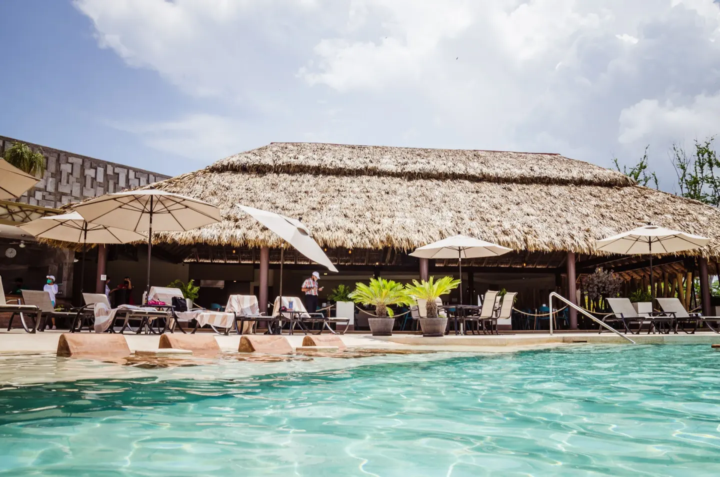 Pool with umbrellas and a large thatched pavilion at Binniguenda Huatulco & Beach Club.
