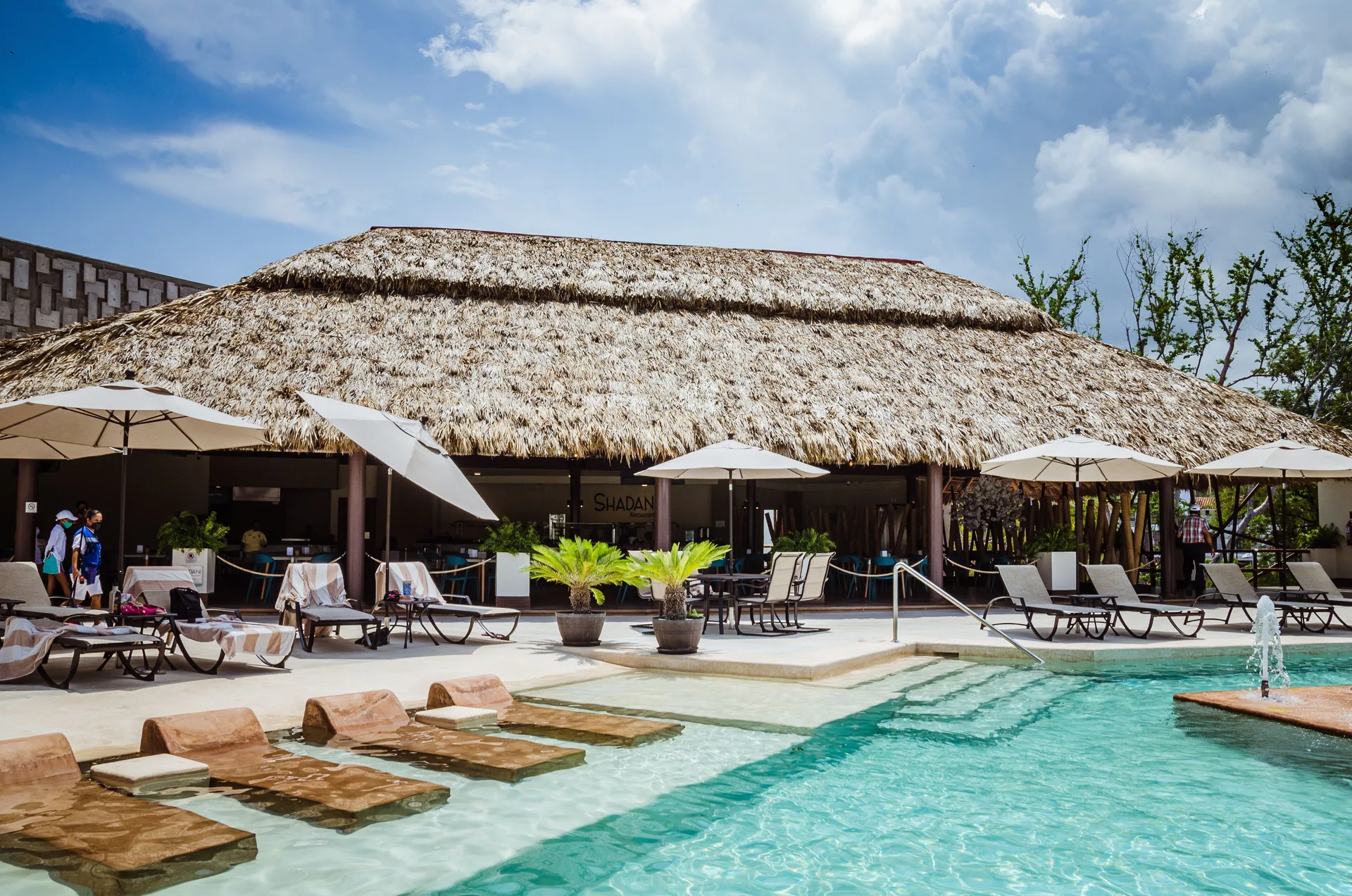 Pool, loungers, umbrellas, and thatched pavilion at Binniguenda Huatulco & Beach Club.
