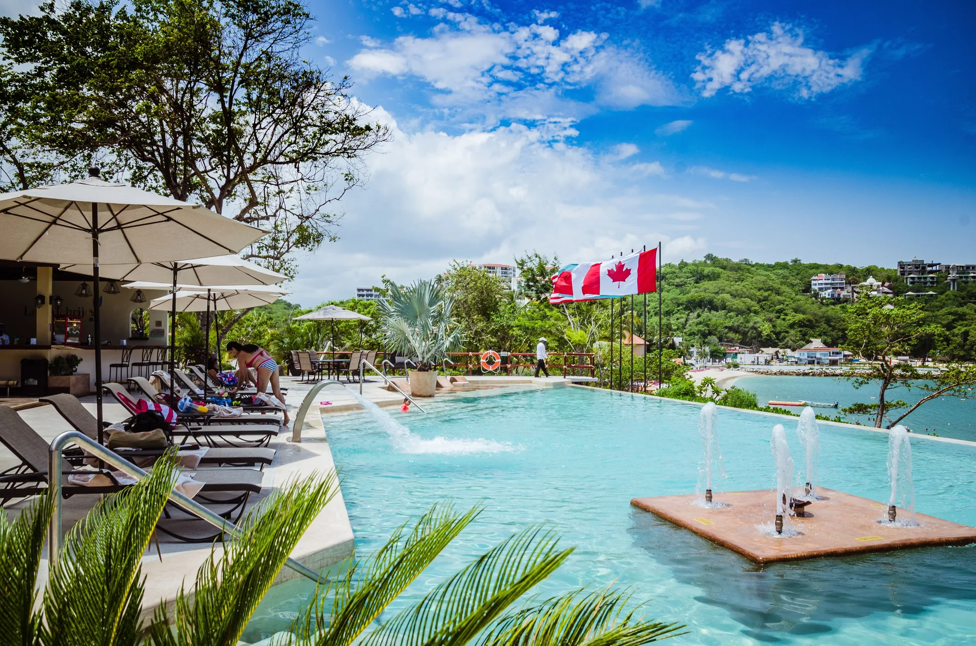 Pool deck with loungers, umbrellas, and bay view at Binniguenda Huatulco & Beach Club.