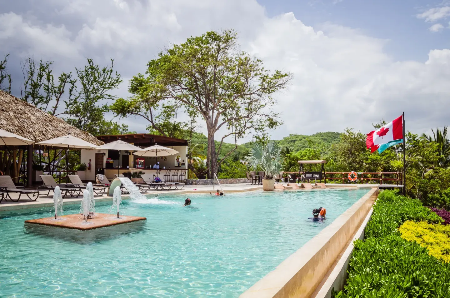 Pool with fountains, loungers, and hillside greenery at Binniguenda Huatulco & Beach Club.