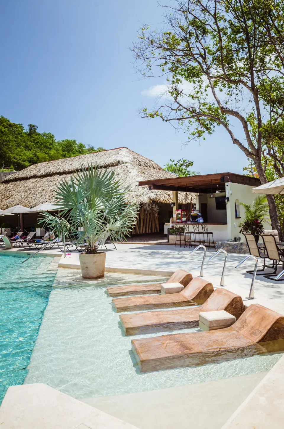 In-water loungers and a thatched pool bar at Binniguenda Huatulco & Beach Club.