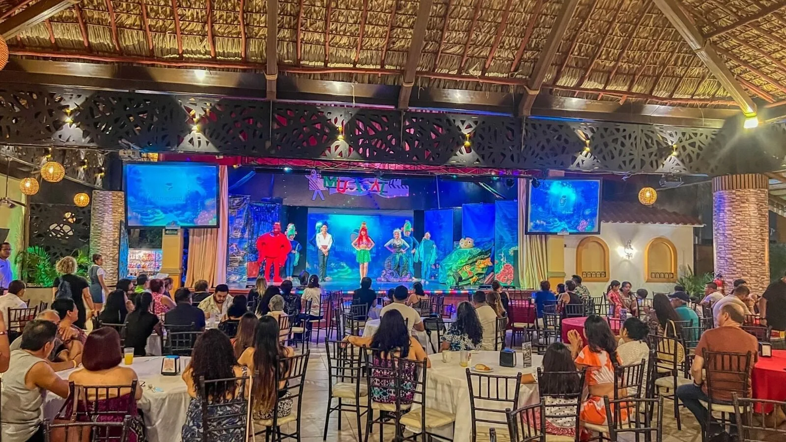 Audience watching a colorful stage show under a palapa roof at Binniguenda Huatulco & Beach Club.