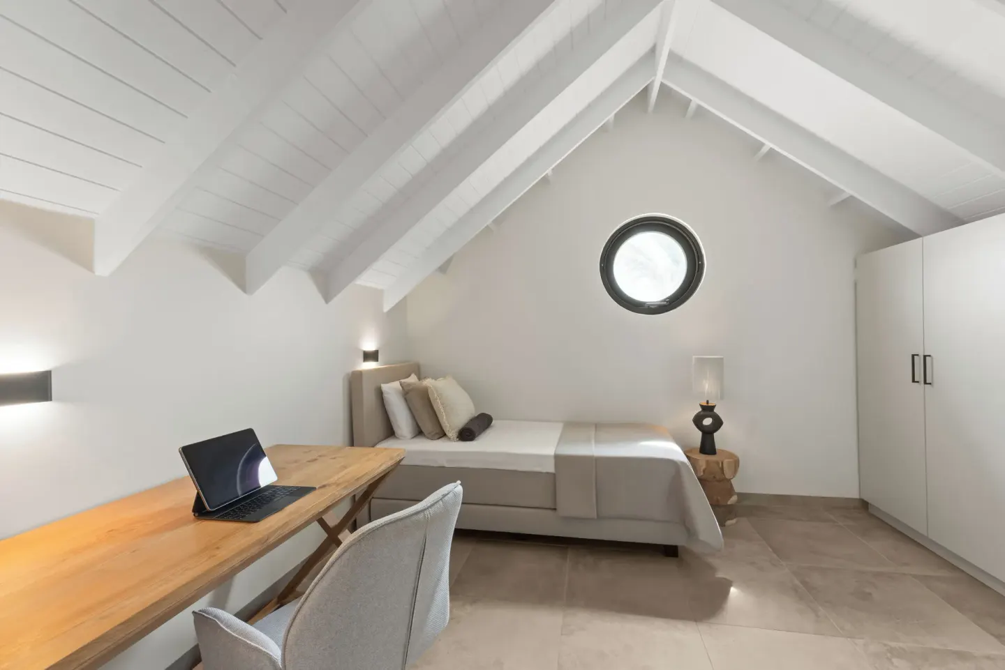 Loft guest room with twin beds, desk, and round window at Blue Bay Curacao Golf & Beach Resort.