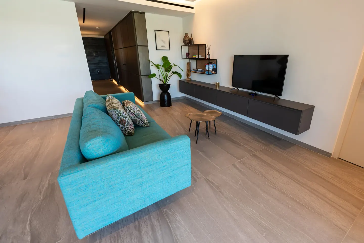 Modern sitting area with turquoise sofa and wall-mounted TV at Blue Bay Curacao Golf & Beach Resort.