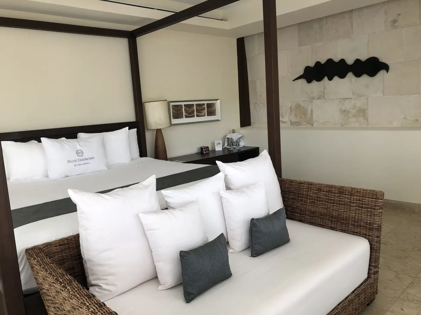 Canopy bed and wicker sofa with pillows in a guest room at Blue Diamond Luxury Boutique.
