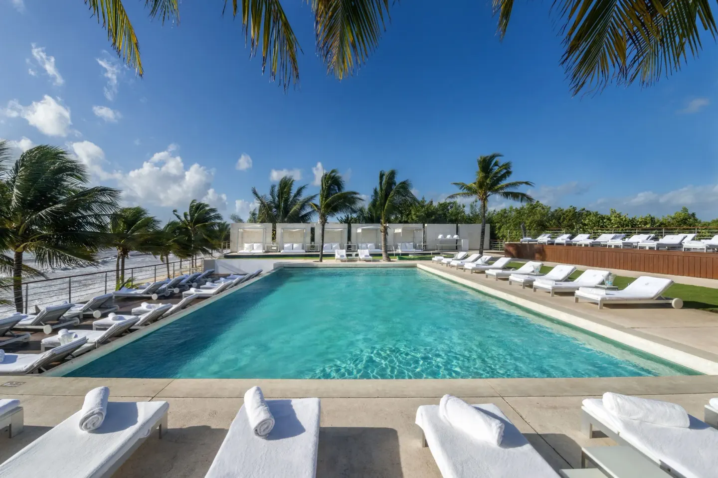 Main pool at Blue Diamond Luxury Boutique with rows of white loungers beside the ocean.
