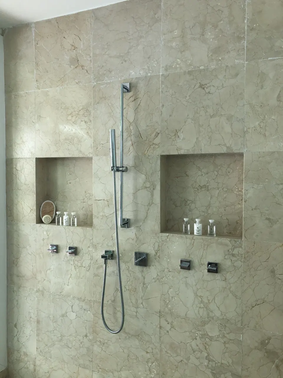 Marble shower wall with handheld fixture and bath amenities at Blue Diamond Luxury Boutique.