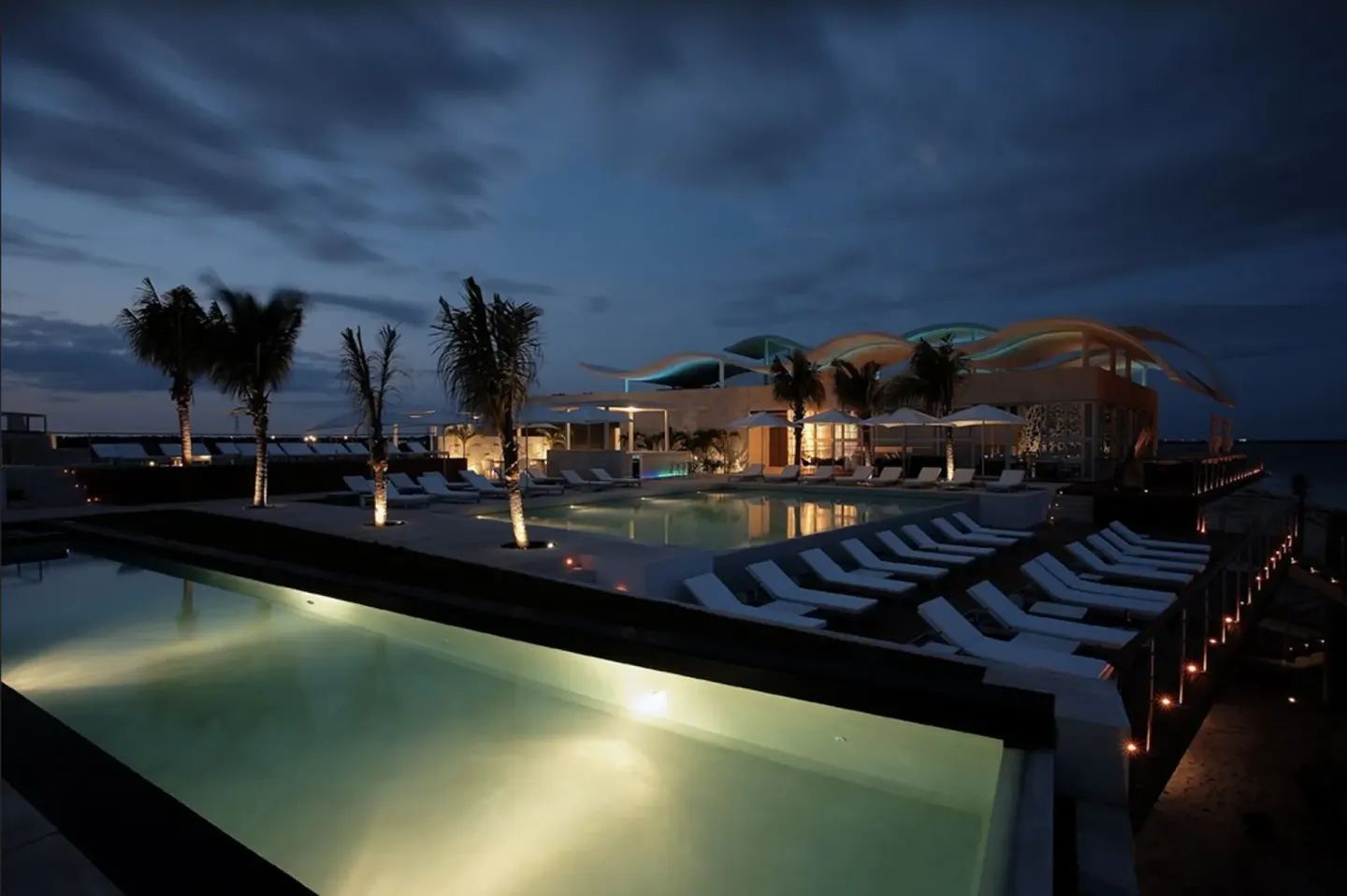 Nighttime resort pool deck at Blue Diamond Luxury Boutique with illuminated water and loungers.