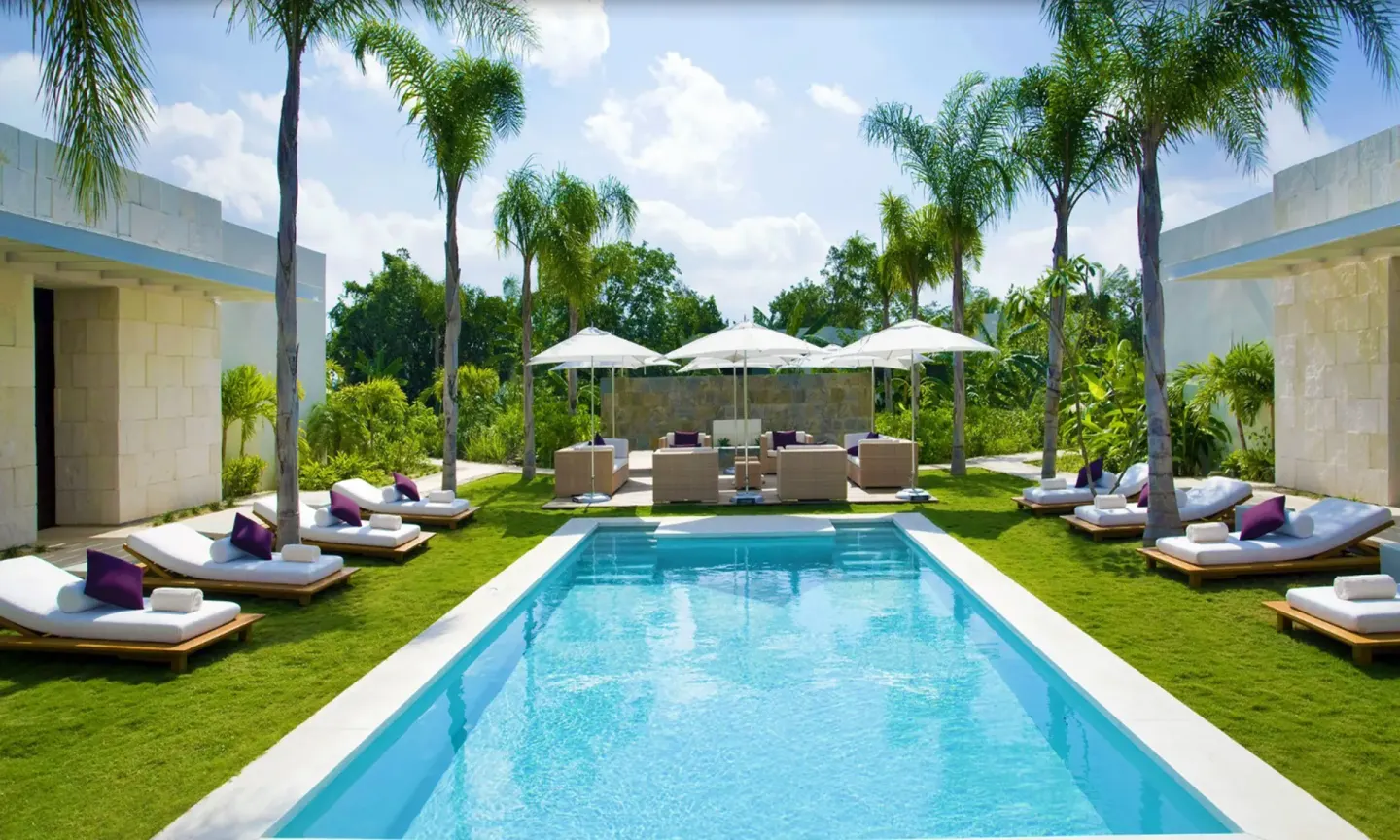 Sunny palm-lined pool courtyard at Blue Diamond Luxury Boutique with loungers and white umbrellas.