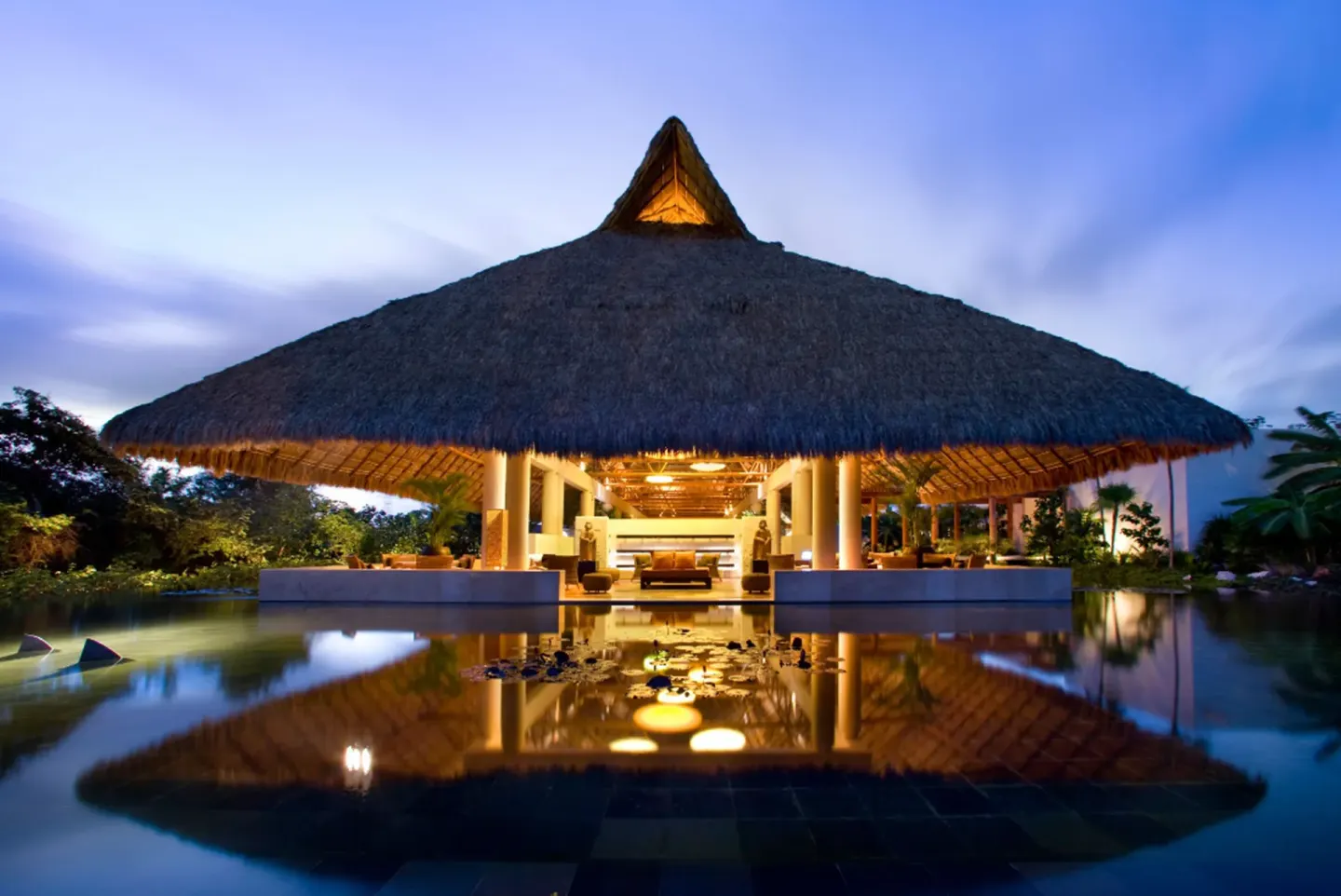 Illuminated thatched pavilion reflected in water at Blue Diamond Luxury Boutique.