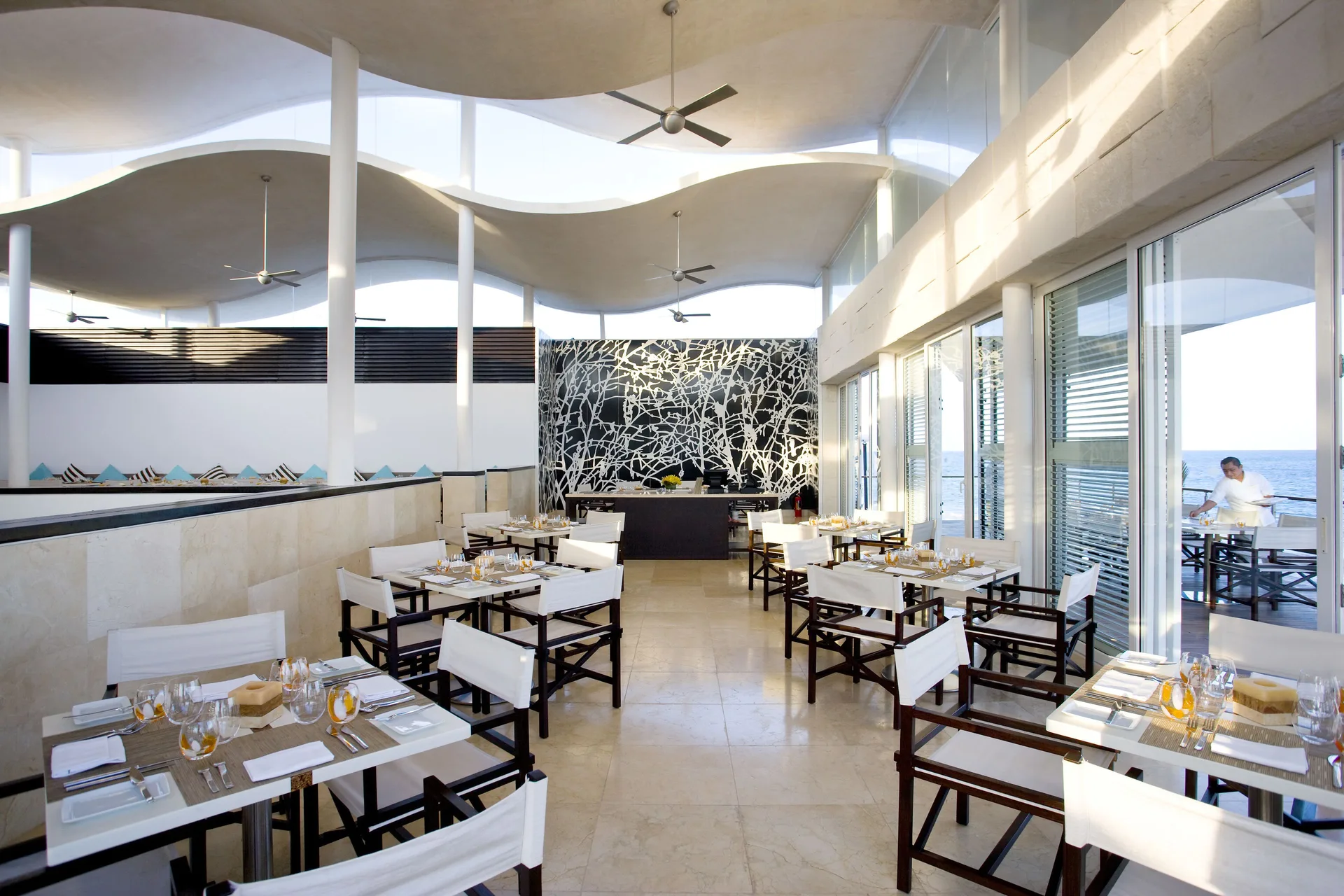 A bright dining room with set tables faces the ocean at Blue Diamond Luxury Boutique.