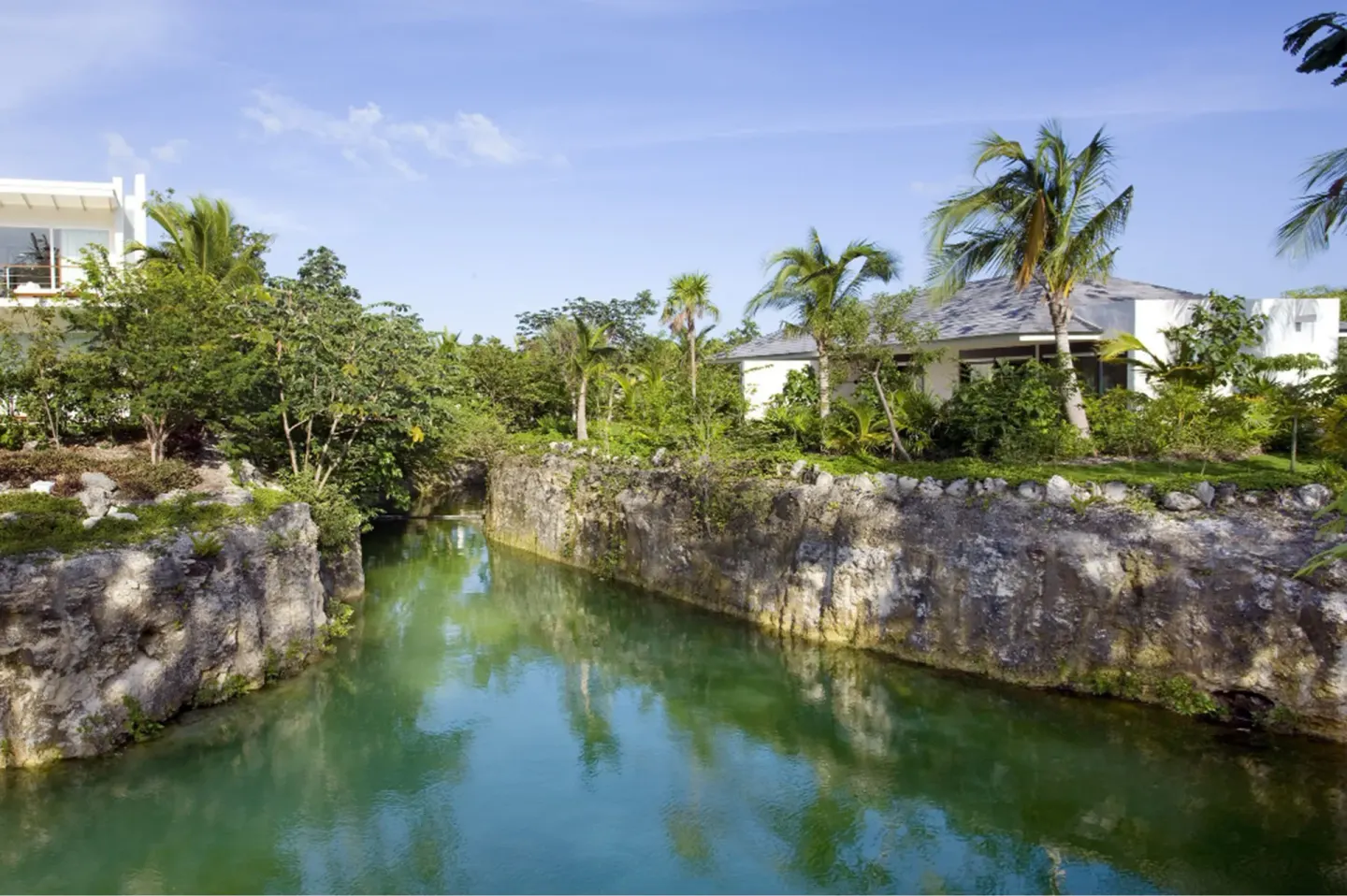 Cenote lagoon and suite buildings at Blue Diamond Luxury Boutique framed by palms and rock walls.