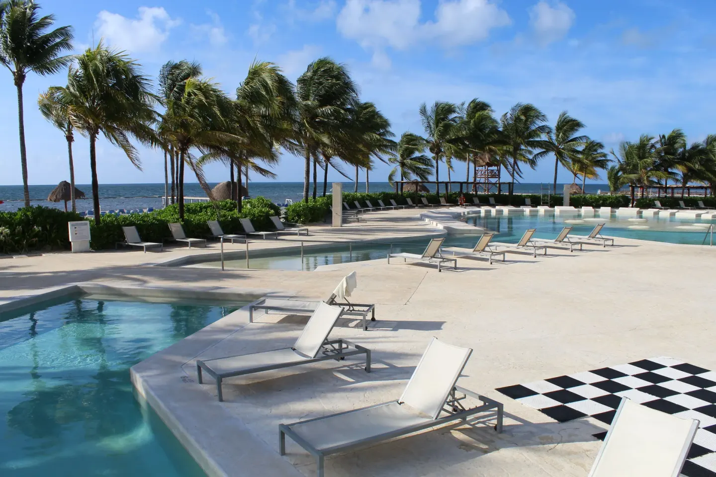 Beachfront pool deck with loungers and palm trees at BlueBay Grand Esmeralda.