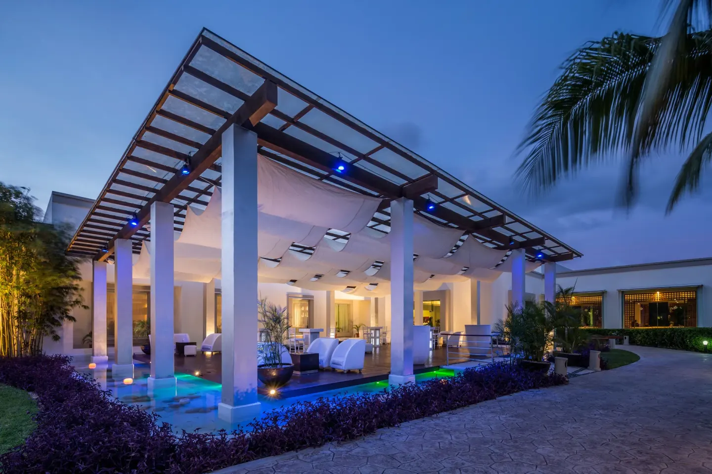 Evening terrace lounge with canopy, blue lighting, and palm at BlueBay Grand Esmeralda.