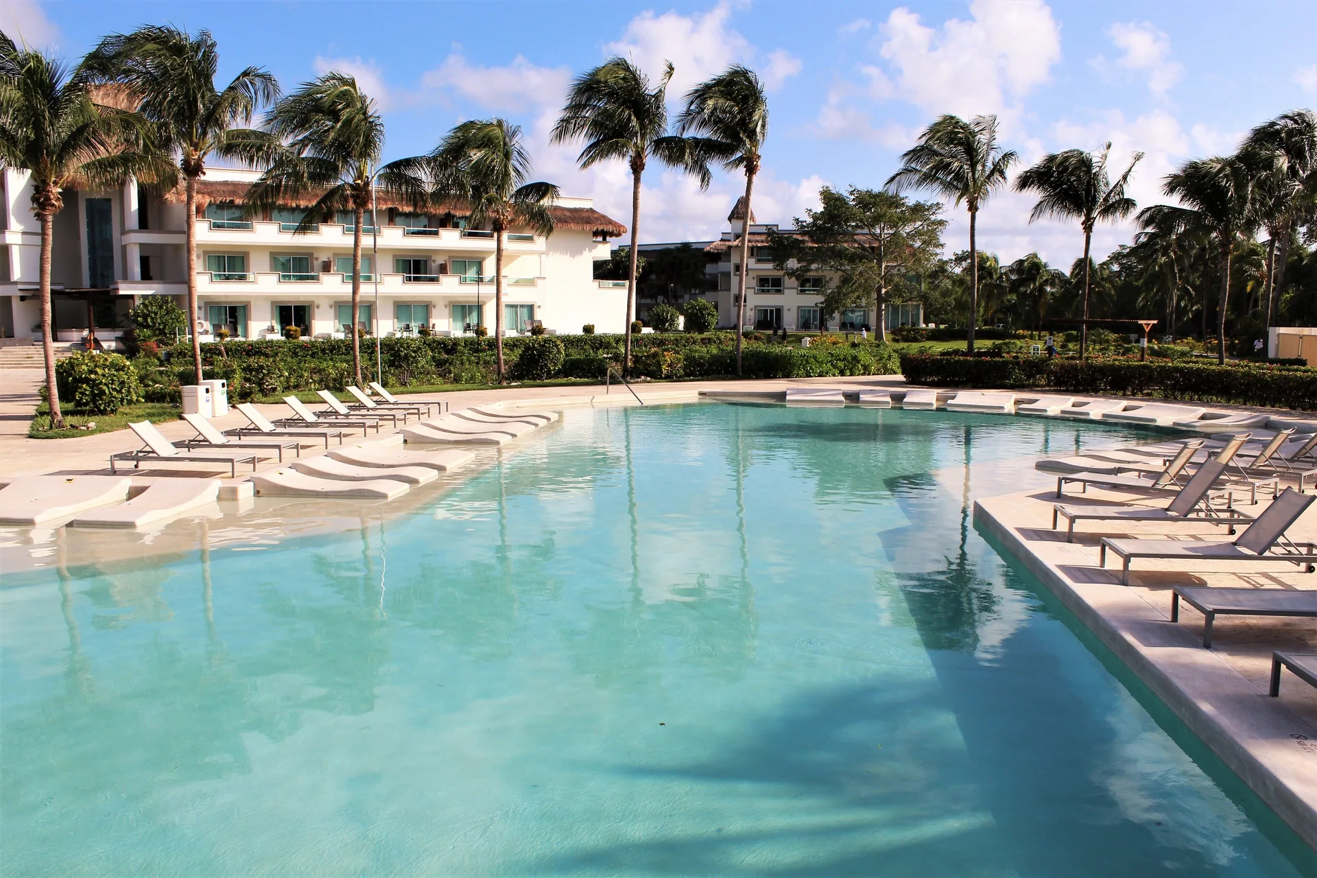 Resort pool with loungers, palms and guest buildings at BlueBay Grand Esmeralda.