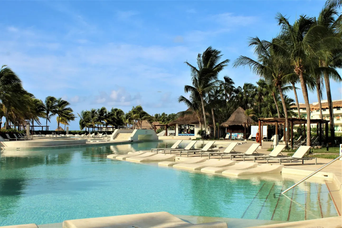 Pool with in-water loungers, palms and thatched cabanas at BlueBay Grand Esmeralda.