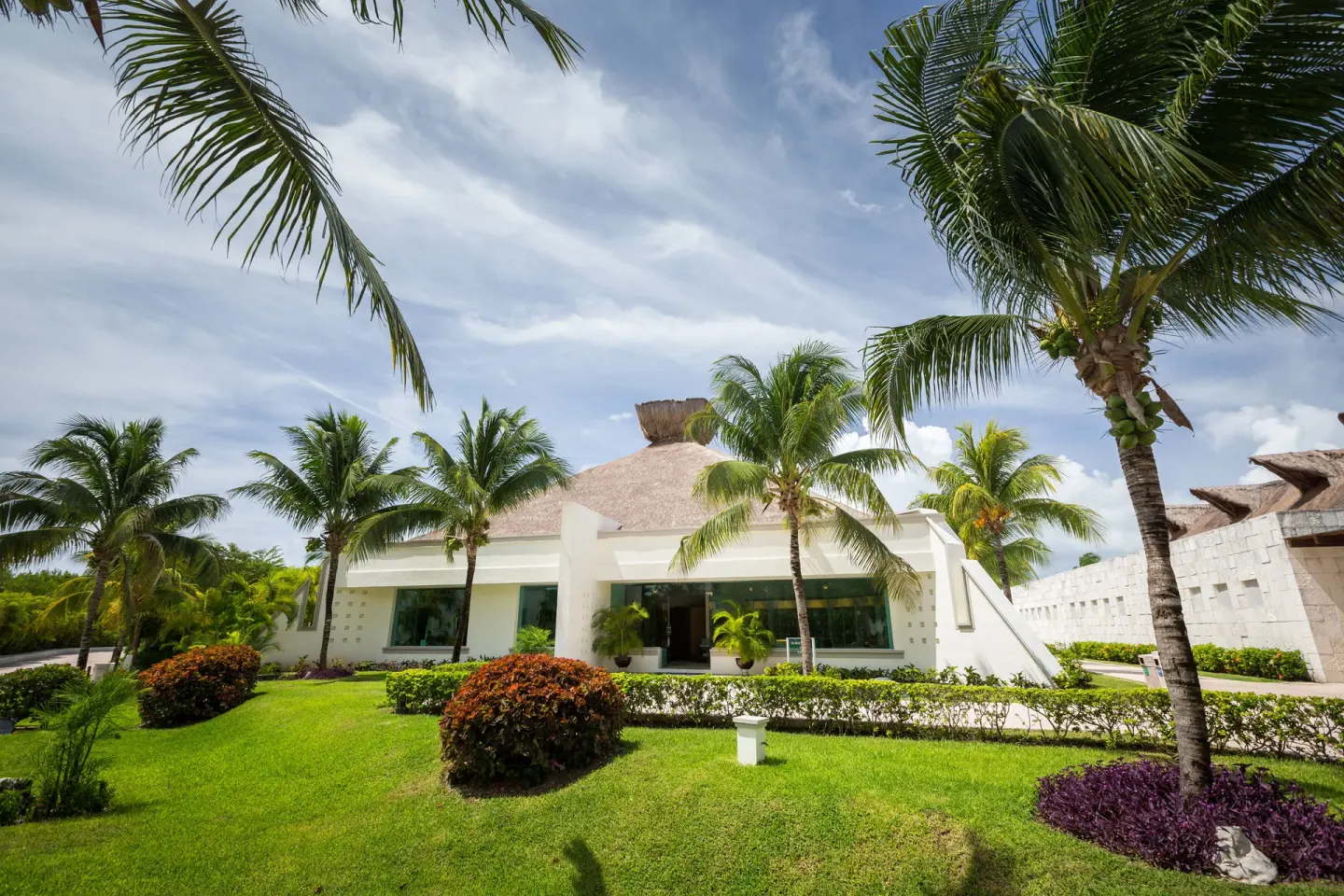 White thatched-roof resort building among palms at BlueBay Grand Esmeralda.