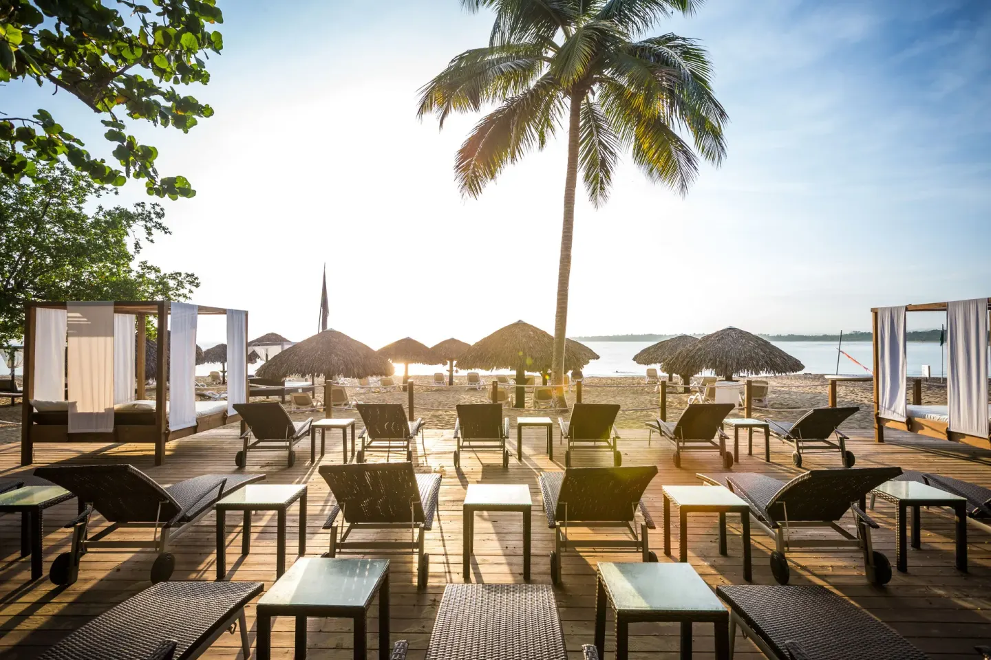 Beach loungers and cabanas face the sea beneath palms at BlueBay Villas Doradas.
