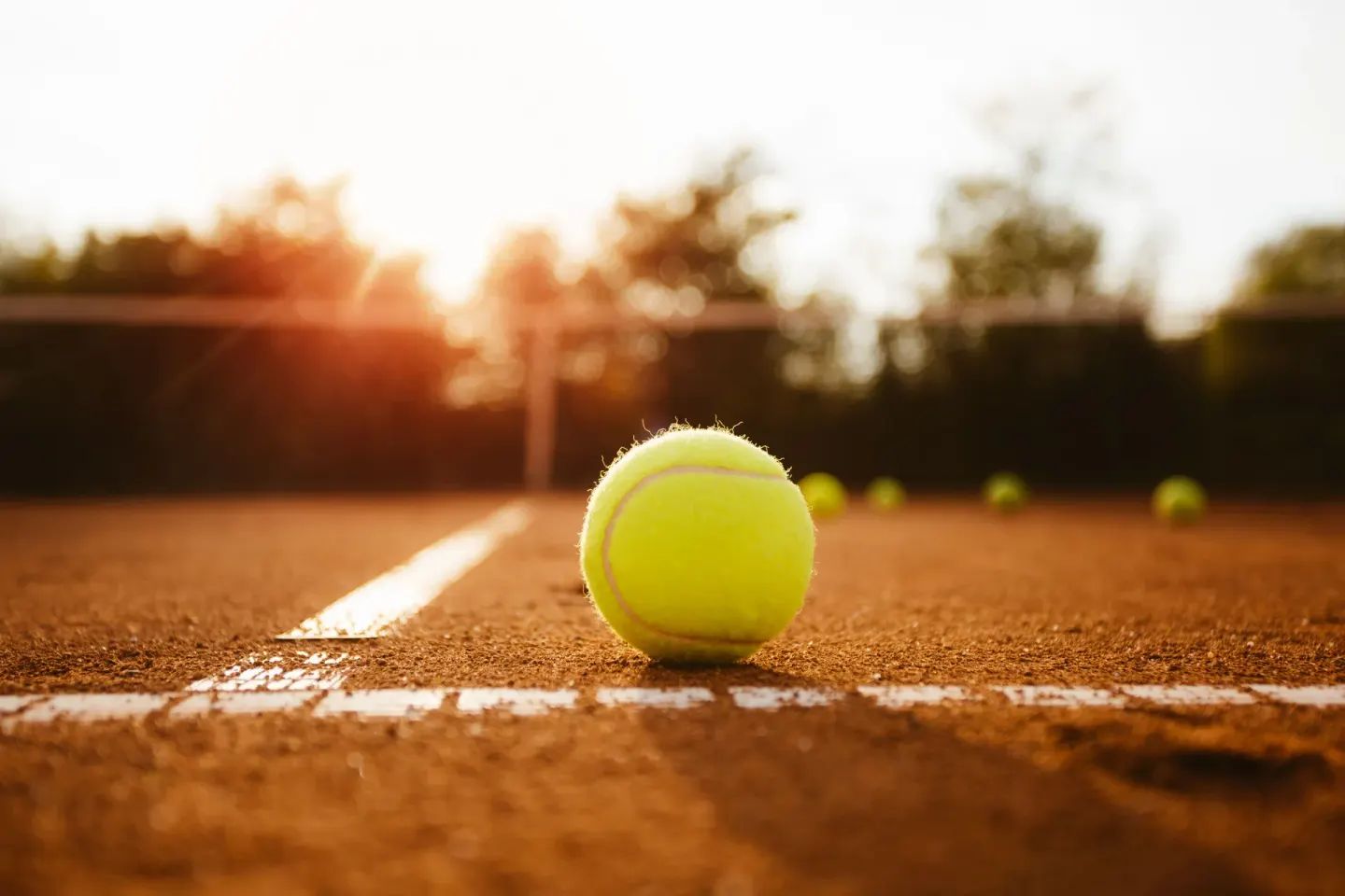 Tennis ball rests on a clay court line in golden light at BlueBay Villas Doradas.