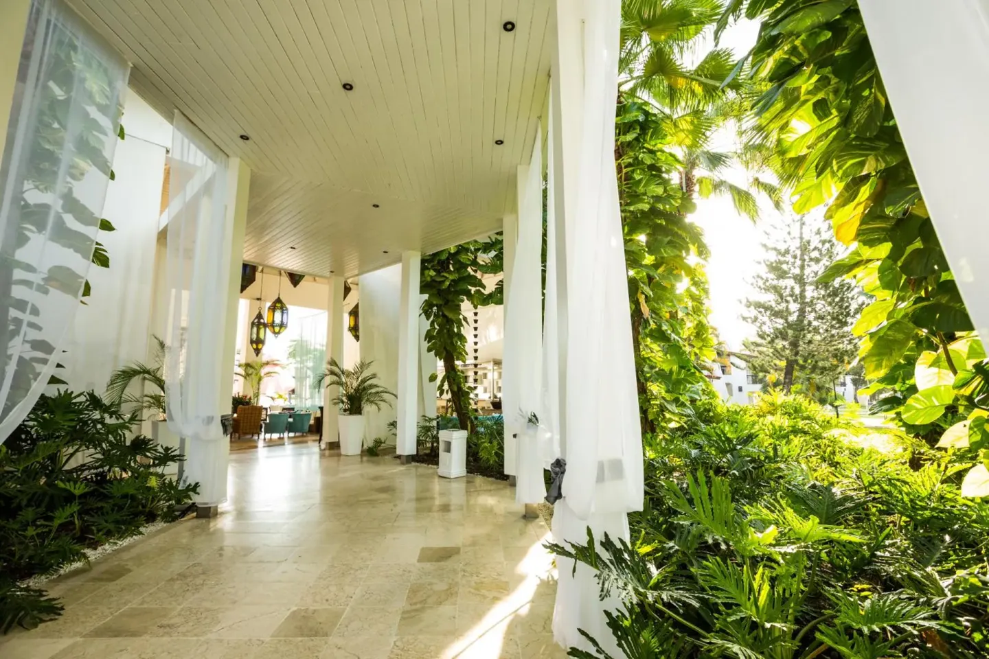 Covered resort walkway with white curtains and tropical gardens at BlueBay Villas Doradas.