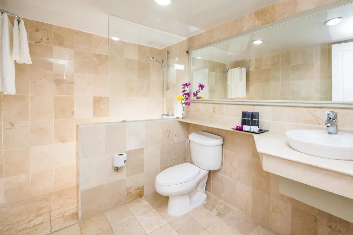 Guest bathroom with beige tile, tub, toilet, sink, and mirror at BlueBay Villas Doradas.