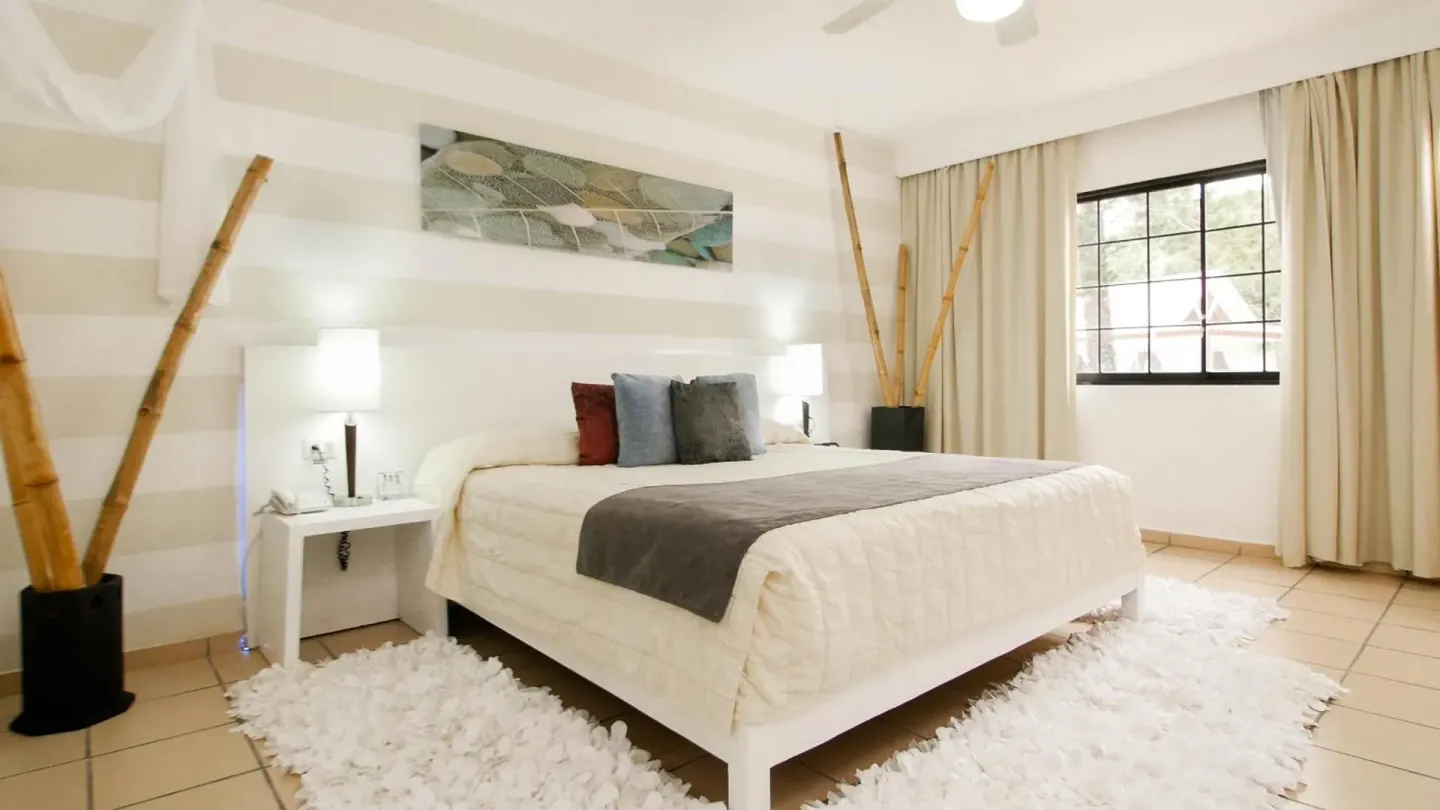 Guest room with a white king bed and bamboo decor at BlueBay Villas Doradas.