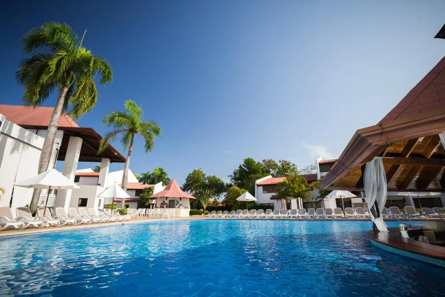 Swimming pool with lounge chairs, palms, and resort buildings at BlueBay Villas Doradas.