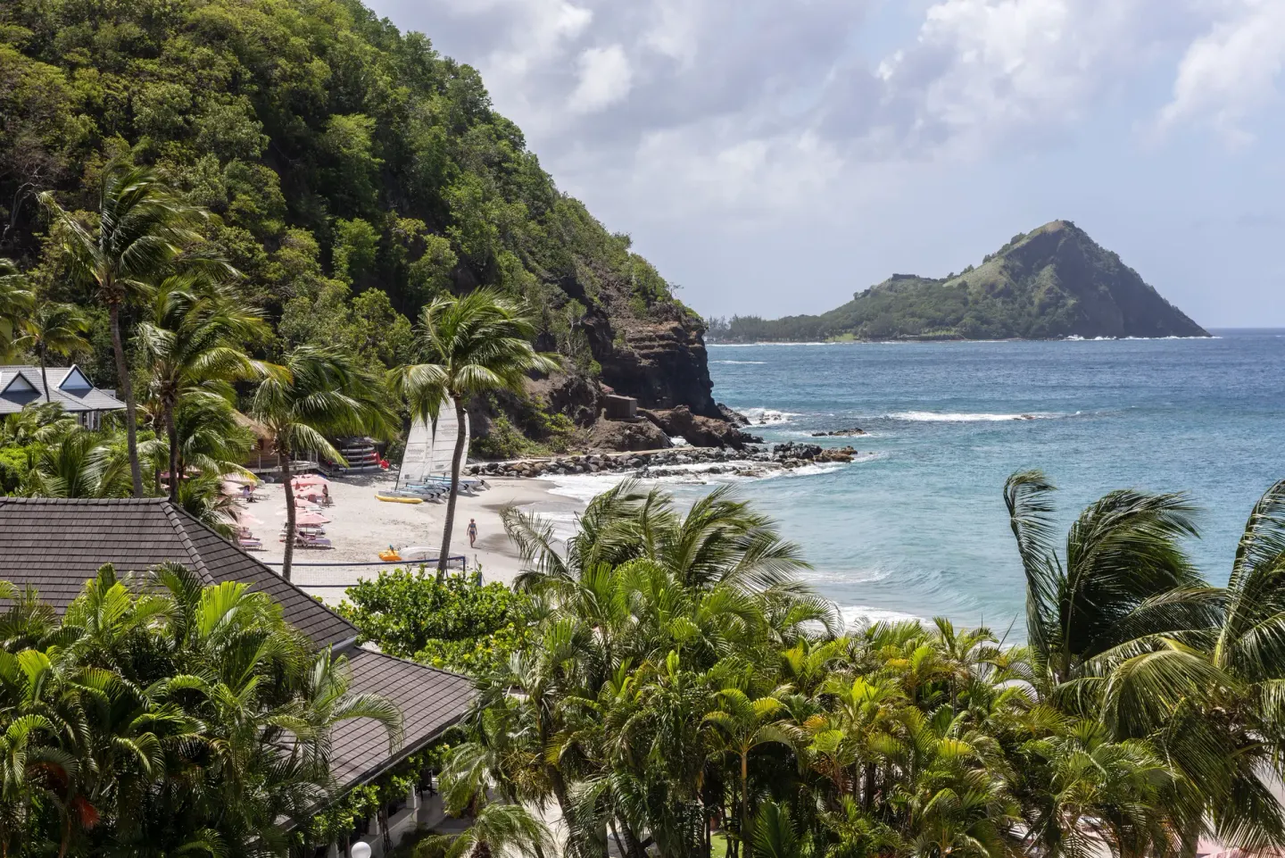 BodyHoliday coastal view with palm trees, beach, rocky cliffs, and blue sea.