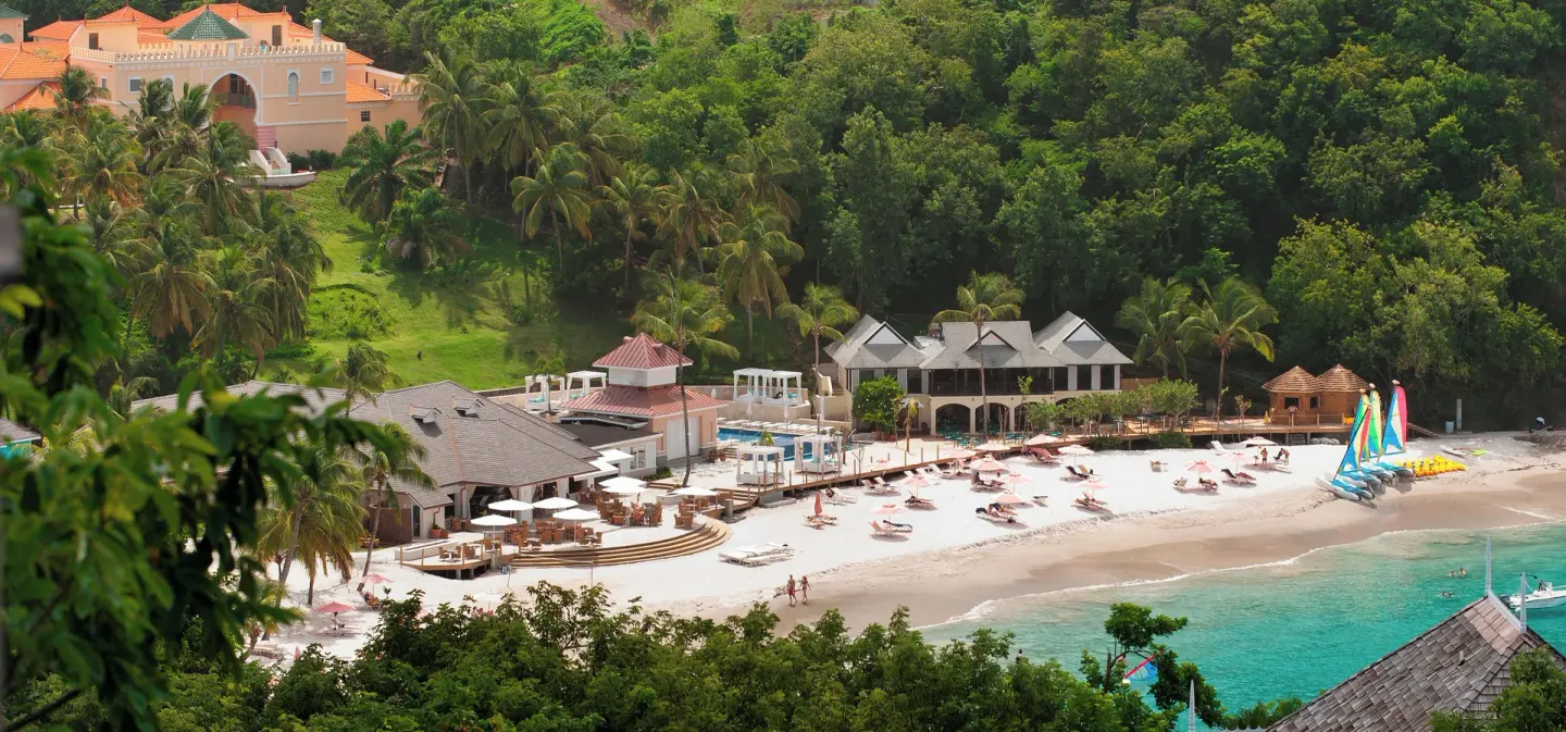 Aerial view of the beachfront, turquoise water, and hillside buildings at BodyHoliday.